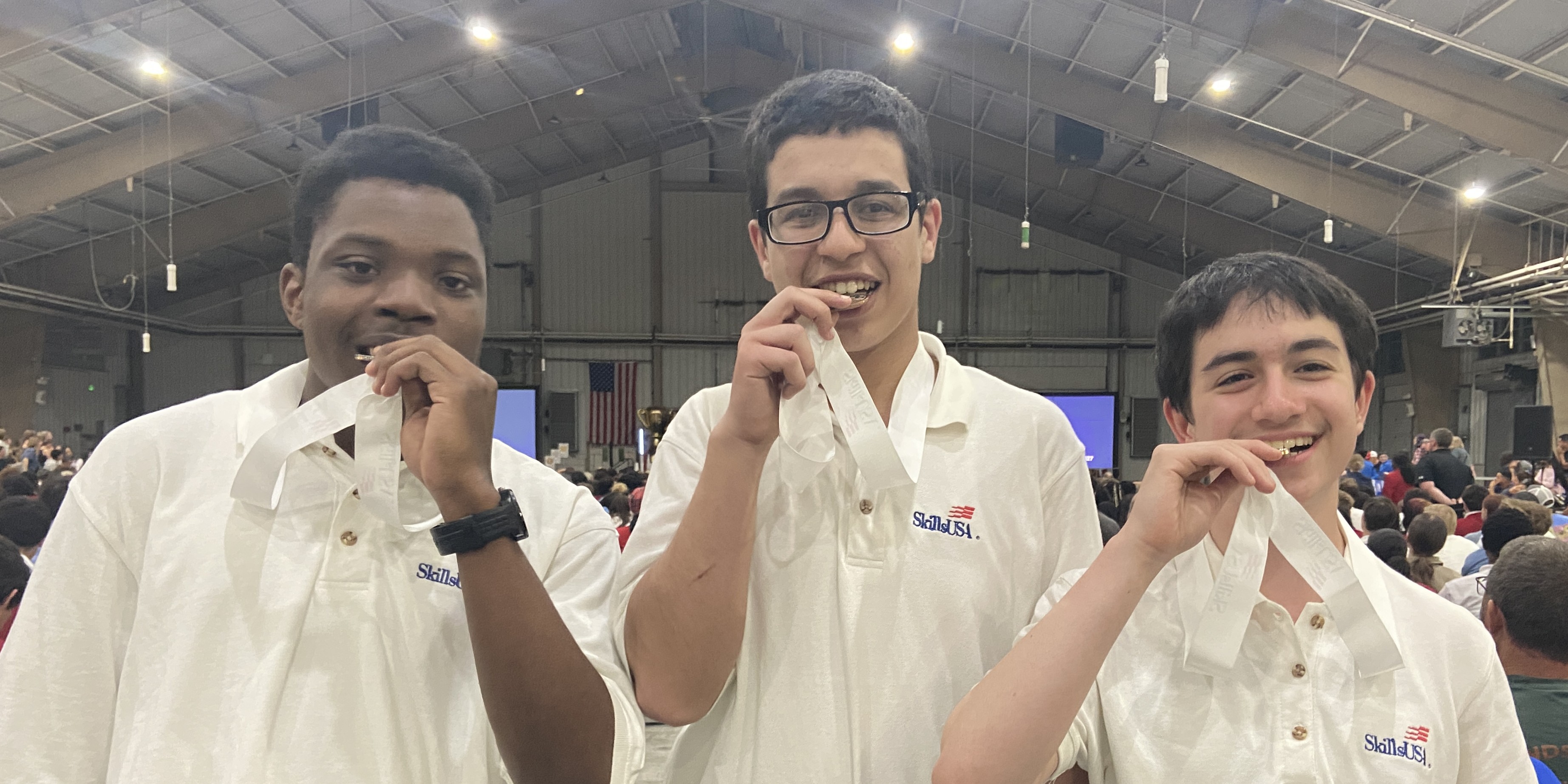 A photo of three students biting medals in white SkillsUSA polos